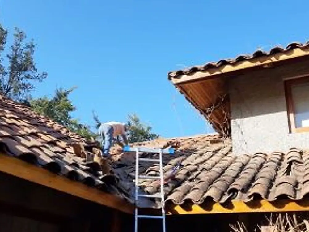 Trabajador de Techos León sobre un techo de teja, junto a una escalera, en El Melocotón