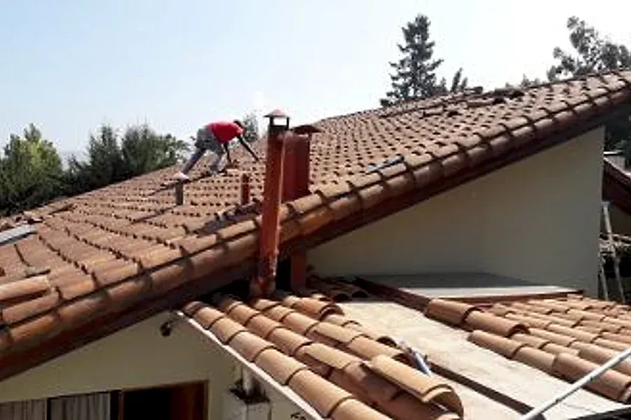 Trabajador sobre un techo de teja junto a una chimenea en Chicureo