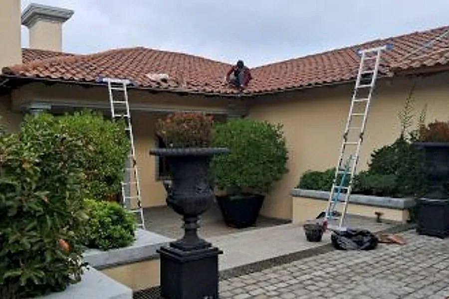 Trabajador sobre un techo de teja colonial, con escaleras apoyadas en una casa de Las Condes
